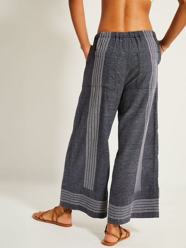 Back of a Woman Standing Wearing lemlem DESTA Pants featuring chambray navy color accented with fine, textured white stripes
