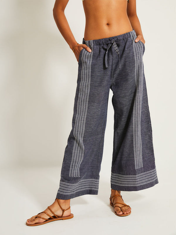 Close up on a Woman Standing Wearing lemlem DESTA Pants featuring chambray navy color accented with fine, textured white stripes
