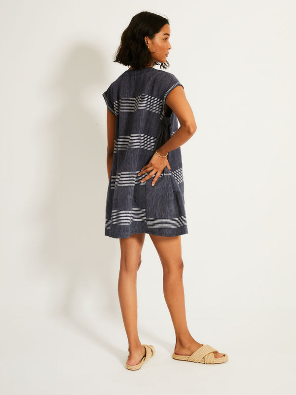 Back of a Woman Standing Wearing lemlem ELINA Caftan featuring chambray navy color accented with fine, textured white stripes
