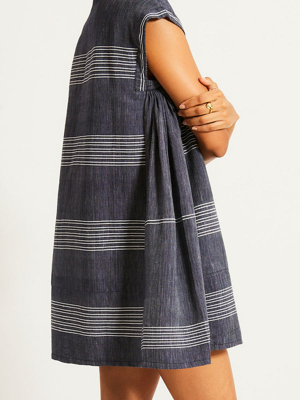 Side close up on a Woman Standing Wearing lemlem ELINA Caftan featuring chambray navy color accented with fine, textured white stripes
