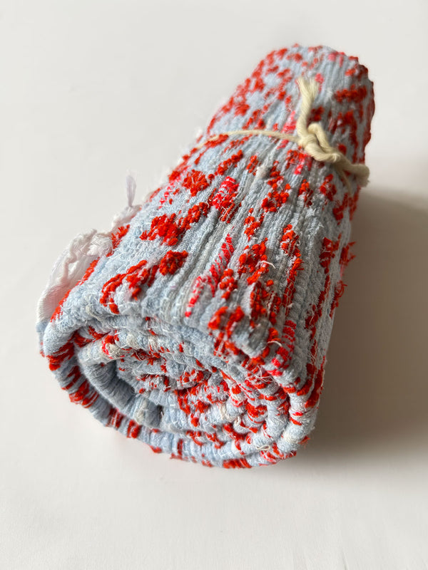 Rolled lemlem Tiki Skypop rug featuring Orange Red and Pale Blue Colors