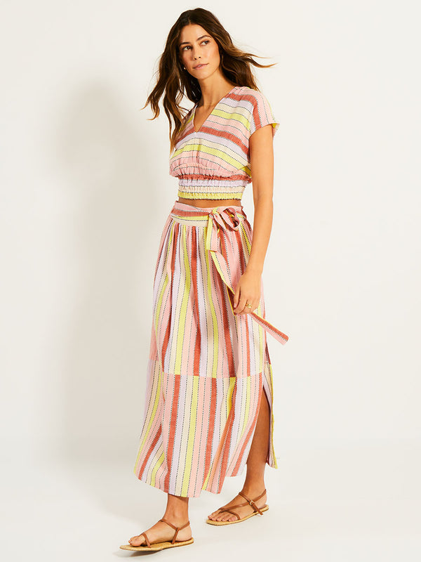 Side Shot of a Woman Standing Wearing lemlem ALIA Plunge Top featuring soft sorbet-colored stripes in shades of peach, rust, and orchid, accented with a citrus yellow pop.
