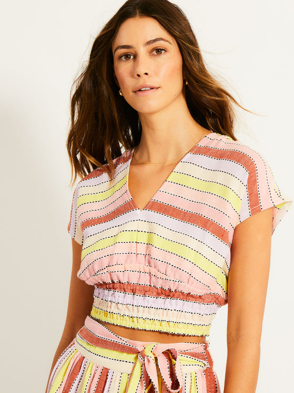 Close up on a Woman Standing Wearing lemlem ALIA Plunge Top featuring soft sorbet-colored stripes in shades of peach, rust, and orchid, accented with a citrus yellow pop.

