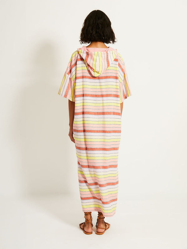 Back of a Woman Standing Wearing lemlem BERITU Hoodied Dress featuring soft sorbet-colored stripes in shades of peach, rust, and orchid, accented with a citrus yellow pop.

