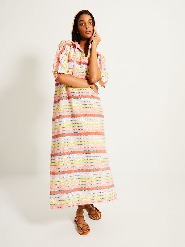 Woman Standing Wearing lemlem BERITU Hoodied Dress featuring soft sorbet-colored stripes in shades of peach, rust, and orchid, accented with a citrus yellow pop.