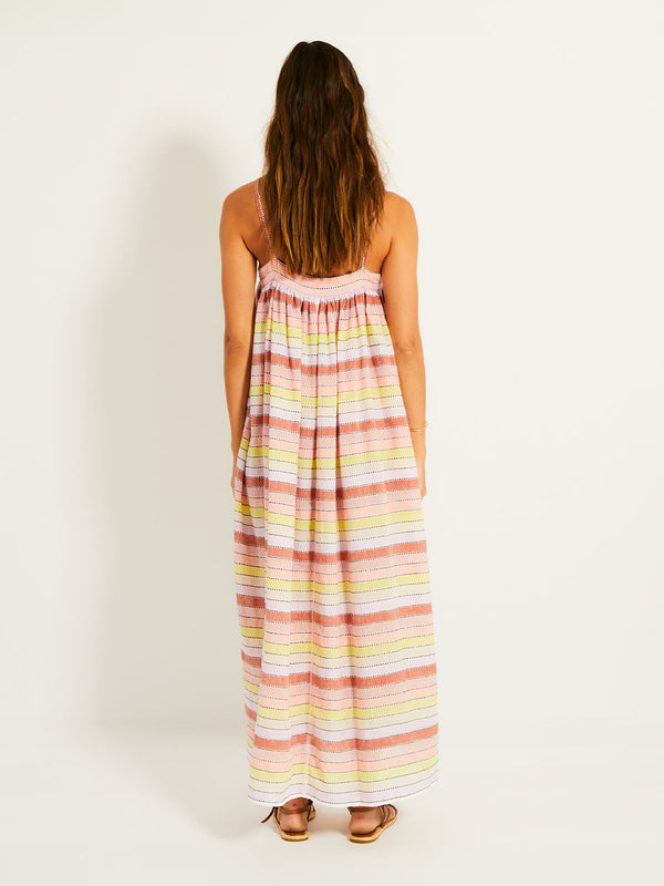 Back of a Woman Standing Wearing lemlem EDA Slip Dress featuring soft sorbet-colored stripes in shades of peach, rust, and orchid, accented with a citrus yellow pop.
