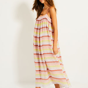 Side Shot of a Woman Standing Wearing lemlem EDA Slip Dress featuring soft sorbet-colored stripes in shades of peach, rust, and orchid, accented with a citrus yellow pop.
