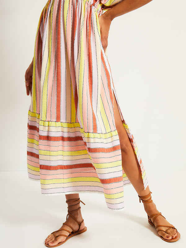 Close up Woman's legs Standing Wearing lemlem LEILA Plunge Dress featuring soft sorbet-colored stripes in shades of peach, rust, and orchid, accented with a citrus yellow pop.
