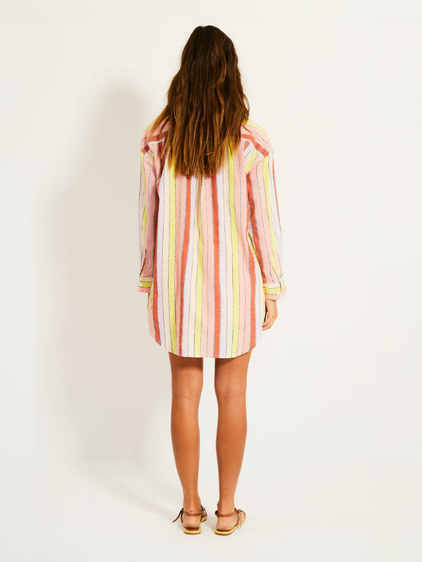 Back of a Woman Standing Wearing lemlem MARIAM Shirt  featuring soft sorbet-colored stripes in shades of peach, rust, and orchid, accented with a citrus yellow pop.
