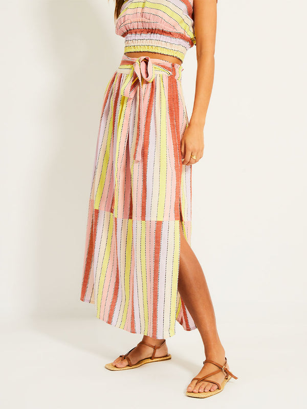 Close up on Woman's legs  Standing Wearing lemlem TOLA SKIRT  featuring soft sorbet-colored stripes in shades of peach, rust, and orchid, accented with a citrus yellow pop.
