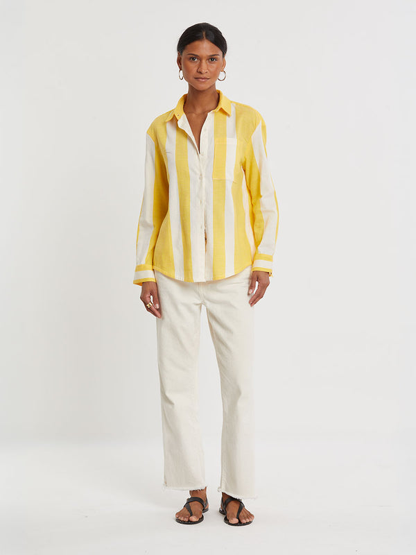 Woman standing wearing lemlem handwoven AISHA Shirt featuring a wide block stripe pattern in rich yellow on a creamy vanilla background.