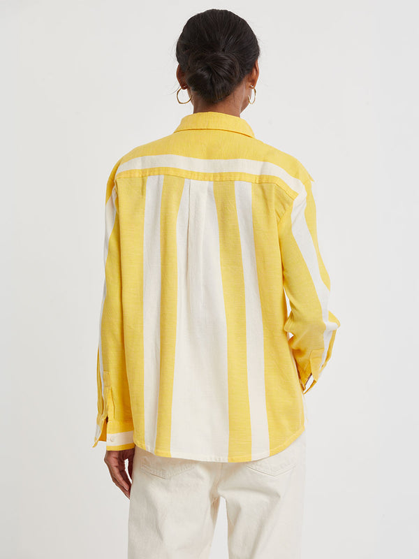 Back of a Woman standing wearing lemlem handwoven AISHA Shirt featuring a wide block stripe pattern in rich yellow on a creamy vanilla background.
