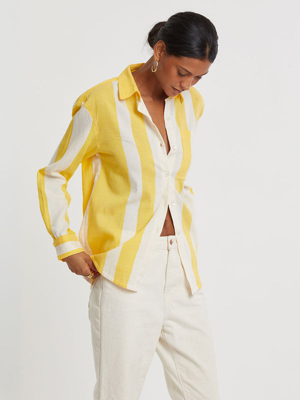 Woman standing wearing lemlem handwoven AISHA Shirt featuring a wide block stripe pattern in rich yellow on a creamy vanilla background.