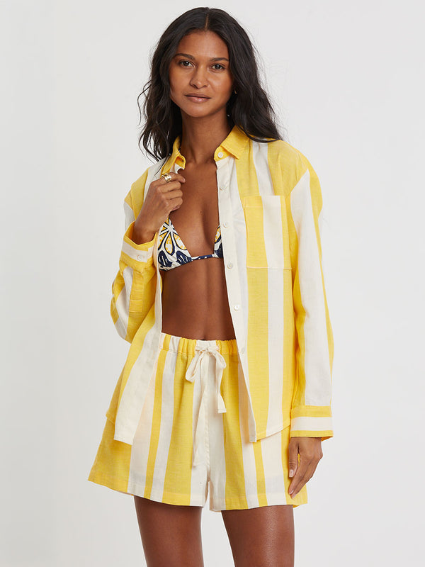 Woman standing wearing lemlem handwoven AISHA Shirt featuring a wide block stripe pattern in rich yellow on a creamy vanilla background.