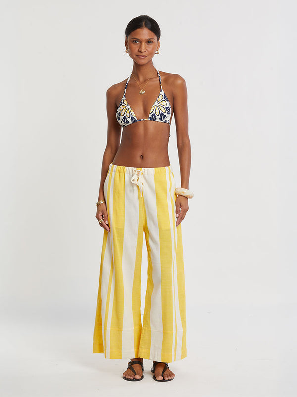 Woman standing wearing lemlem handwoven DESTA Pants featuring a wide block stripe pattern in rich yellow on a creamy vanilla background.