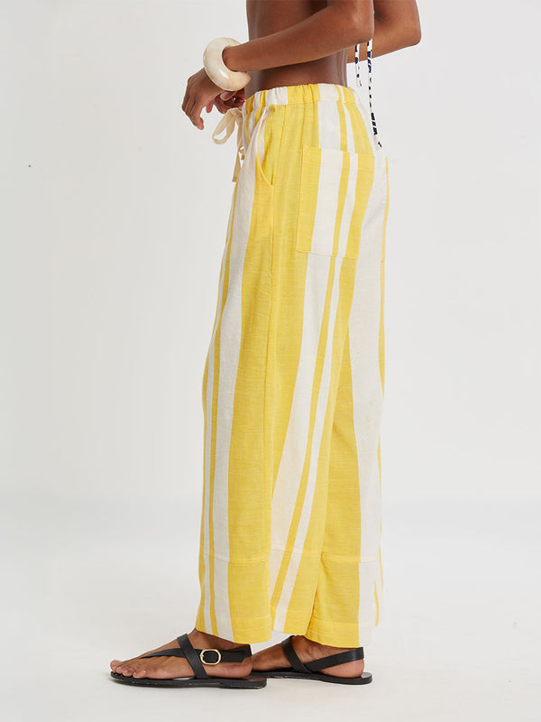 Woman standing wearing lemlem handwoven DESTA Pants featuring a wide block stripe pattern in rich yellow on a creamy vanilla background.
