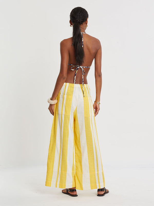 Woman standing wearing lemlem handwoven DESTA Pants featuring a wide block stripe pattern in rich yellow on a creamy vanilla background.