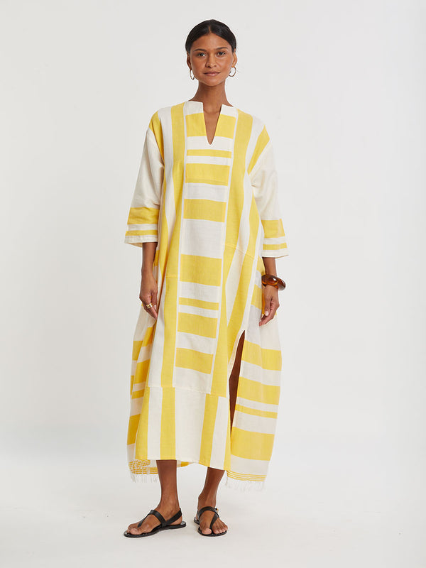 Woman standing wearing lemlem handwoven FANA Caftan featuring a wide block stripe pattern in rich yellow on a creamy vanilla background.