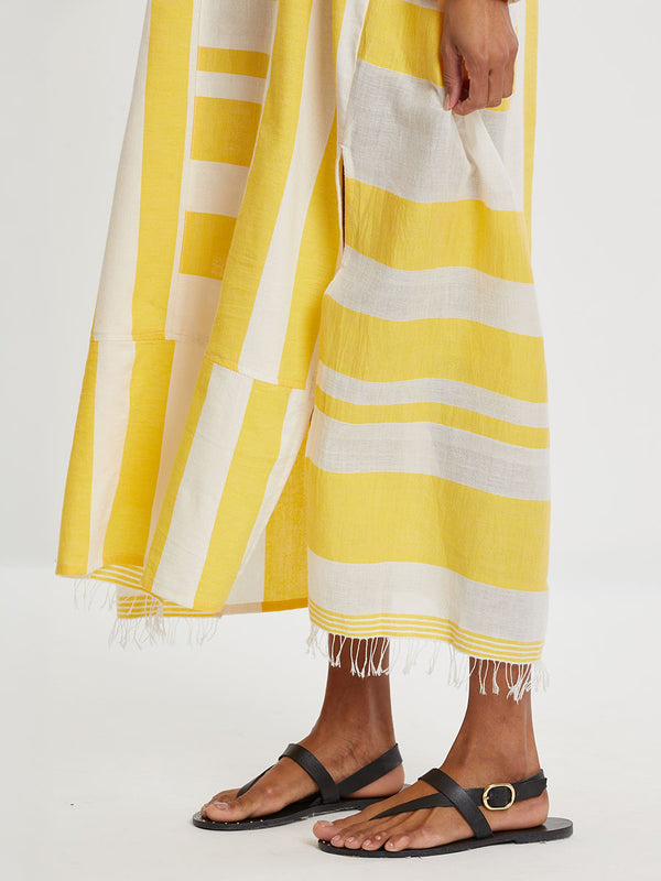Close up on a Woman standing wearing lemlem handwoven FANA Caftan featuring a wide block stripe pattern in rich yellow on a creamy vanilla background.