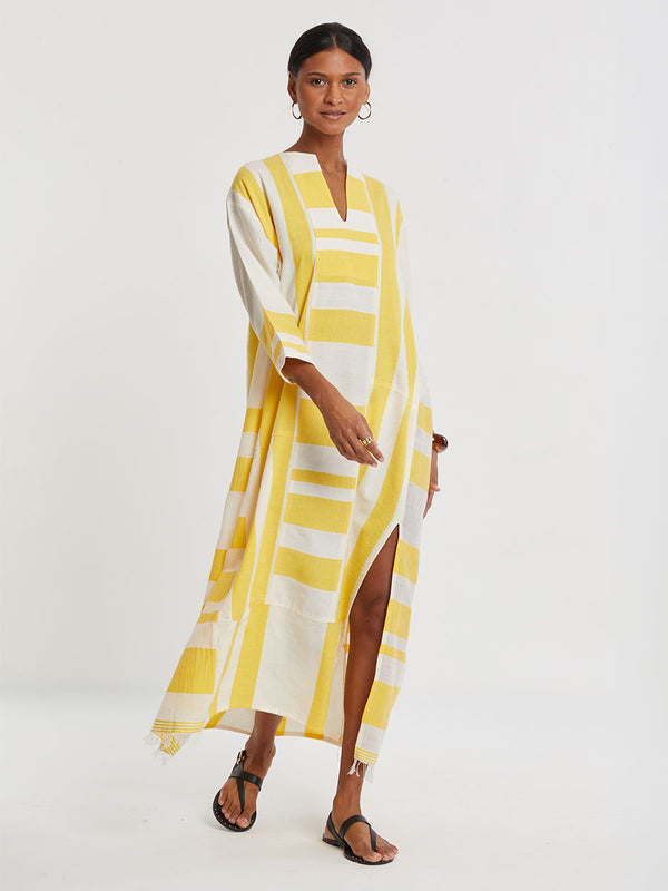 Woman standing wearing lemlem handwoven FANA Caftan featuring a wide block stripe pattern in rich yellow on a creamy vanilla background.
