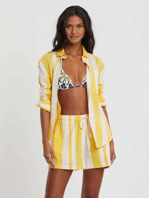 Woman standing wearing lemlem handwoven SAFIA Shorts and AISHA Shirt featuring a wide block stripe pattern in rich yellow on a creamy vanilla background.