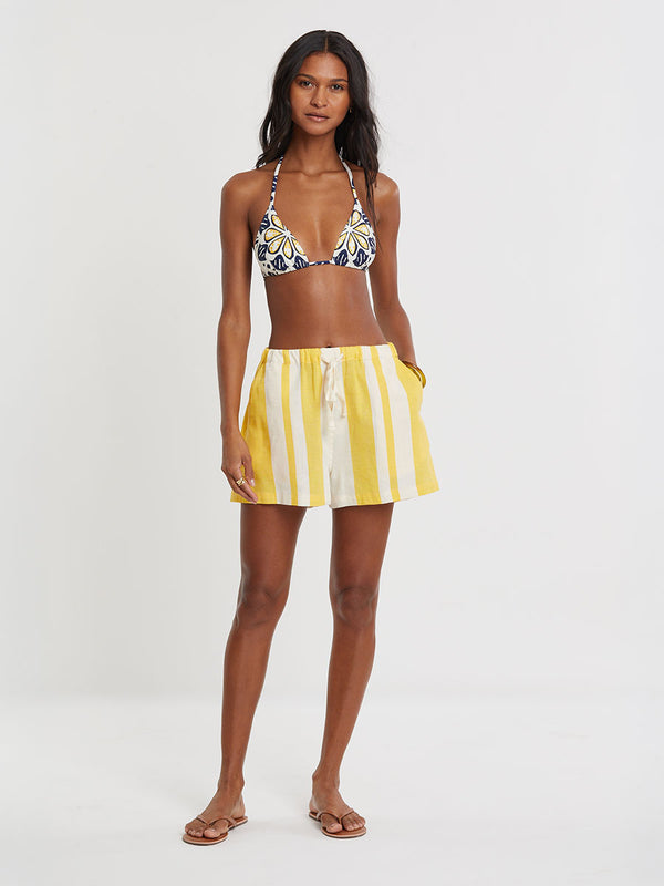 Woman standing wearing lemlem handwoven SAFIA Shorts featuring a wide block stripe pattern in rich yellow on a creamy vanilla background.