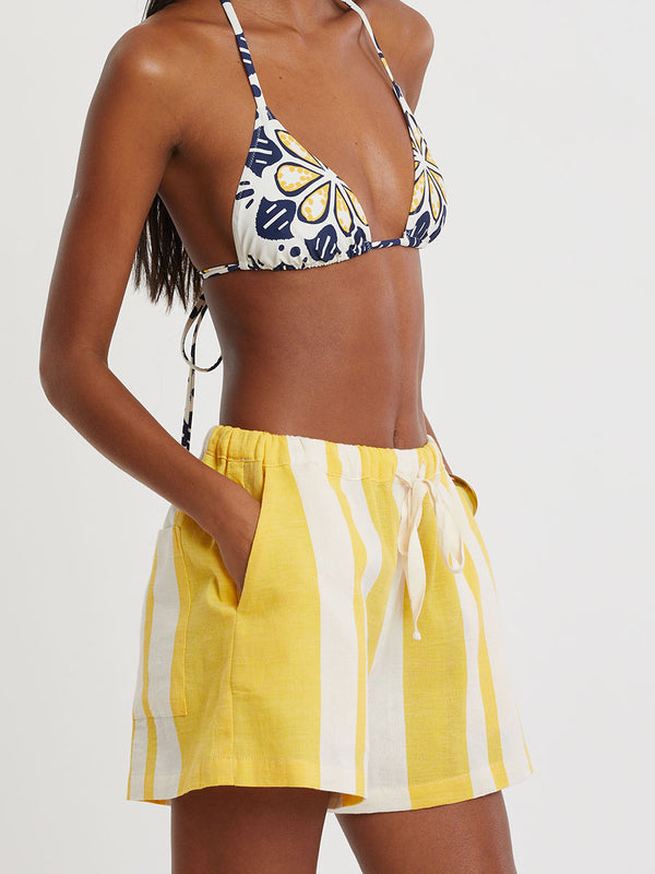 Woman standing wearing lemlem handwoven SAFIA Shorts featuring a wide block stripe pattern in rich yellow on a creamy vanilla background.