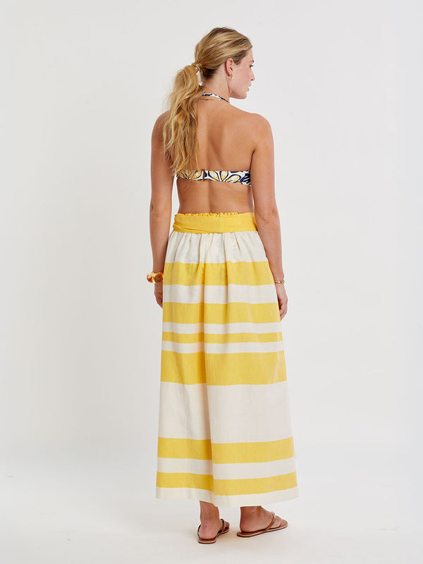 Woman standing wearing lemlem handwoven TOLA Skirt featuring a wide block stripe pattern in rich yellow on a creamy vanilla background.