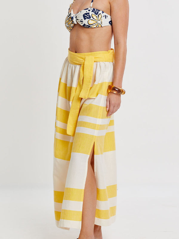 Woman standing wearing lemlem handwoven TOLA Skirt featuring a wide block stripe pattern in rich yellow on a creamy vanilla background.