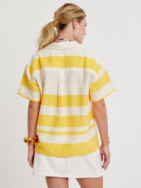 Back of a Woman standing wearing lemlem handwoven TUULI Cabana Shirt featuring a wide block stripe pattern in rich yellow on a creamy vanilla background.