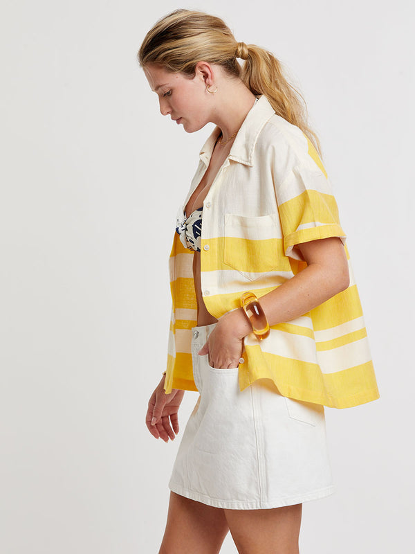 Woman standing wearing lemlem handwoven TUULI Cabana Shirt featuring a wide block stripe pattern in rich yellow on a creamy vanilla background.