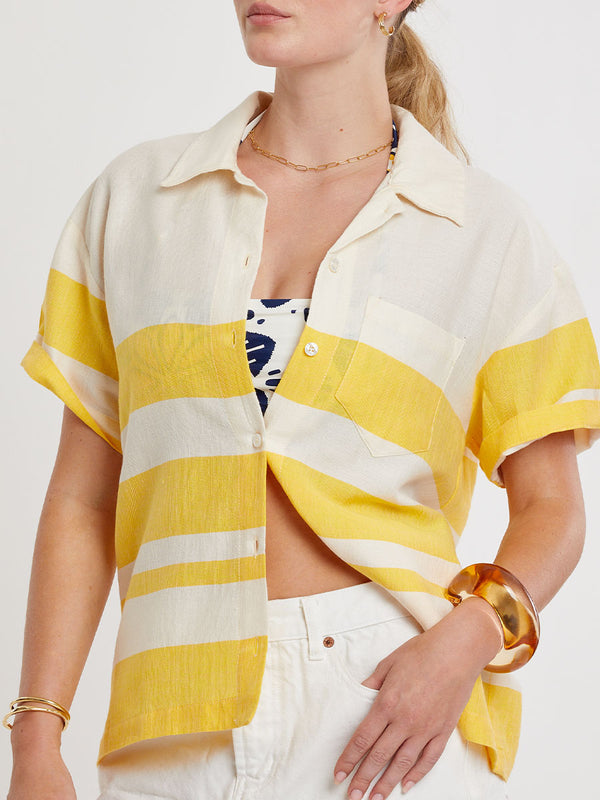 Woman standing wearing lemlem handwoven TUULI Cabana Shirt featuring a wide block stripe pattern in rich yellow on a creamy vanilla background.