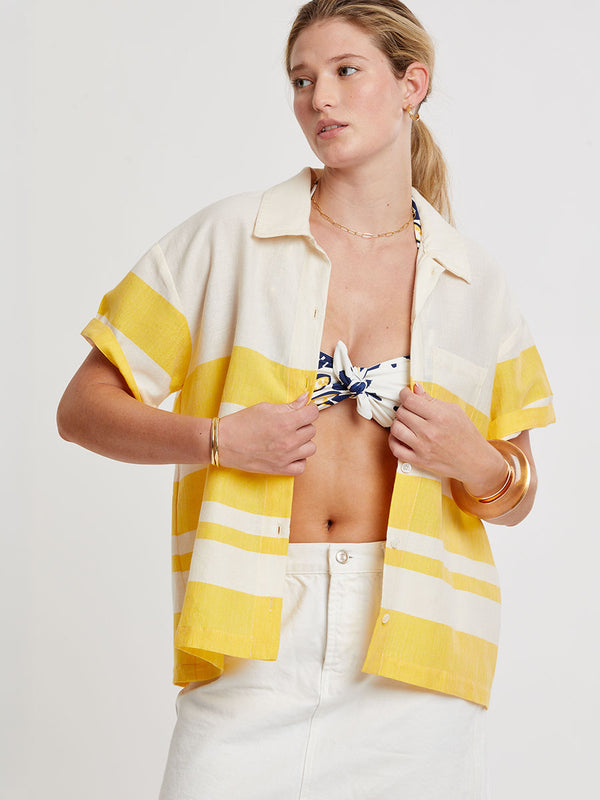 Woman standing wearing lemlem handwoven TUULI Cabana Shirt featuring a wide block stripe pattern in rich yellow on a creamy vanilla background.