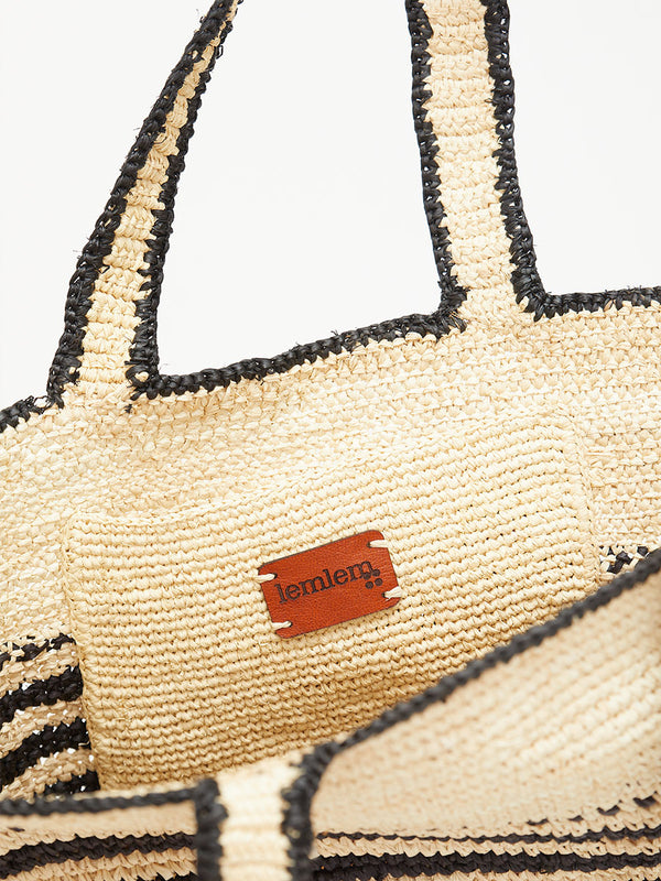 Beige straw bag with black accents and a visible brand logo on a white background