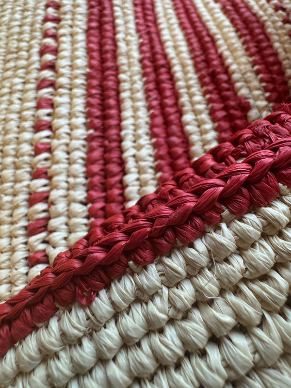 Close-up of a red and beige hand-crocheted raffia tote bag with a braided edge.