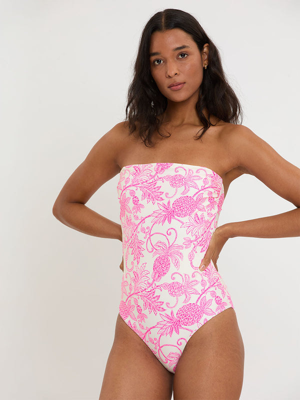 Woman standing wearing lemlem DINHA One Piece featuring a unique custom tropical pineapple motif in vibrant fuchsia on an ivory background.