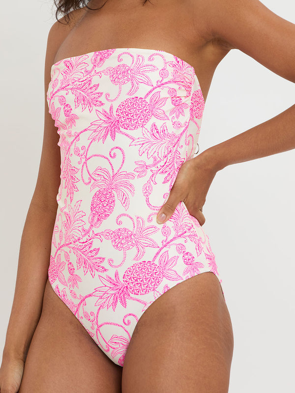 Woman standing wearing lemlem DINHA One Piece featuring pink pineapple pattern on white background