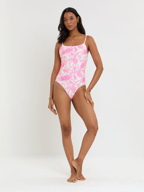 Woman standing wearing lemlem ELENE One Piece featuring a unique custom tropical pineapple motif in vibrant fuchsia on an ivory background.