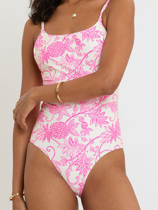 Woman standing wearing lemlem DINHA One Piece featuring pink pineapple pattern on white background