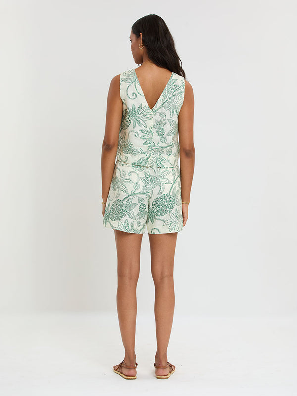 Woman Standing wearing lemlem ADOWA Tank and FAIZAH Shorts featuring a custom, hand-drawn tropical pineapple motif in a tropical green hue on an ivory background.