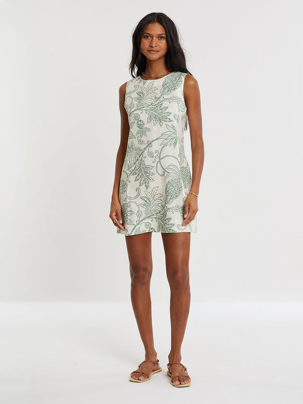 Woman Standing wearing lemlem PERSINA Dress featuring a custom, hand-drawn tropical pineapple motif in a tropical green hue on an ivory background.