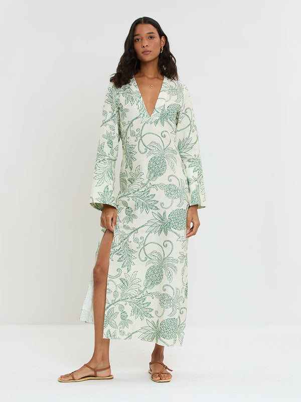 Woman Standing wearing lemlem THEODORA Dress featuring a custom, hand-drawn tropical pineapple motif in a tropical green hue on an ivory background.