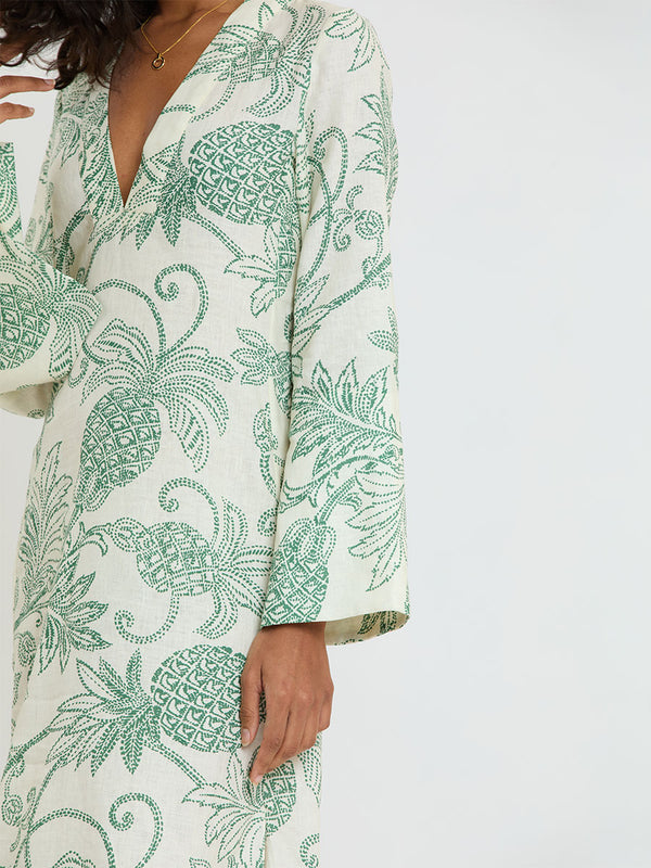 Woman Standing wearing lemlem THEODORA Dress featuring a custom, hand-drawn tropical pineapple motif in a tropical green hue on an ivory background.