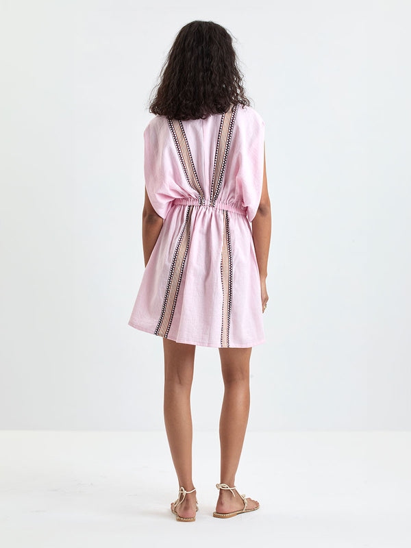 Back of a Woman Standing wearing lemlem ALEM Dress featuring detailed bands of deep burgundy, bronze, and pink stripes beautifully placed on a light cream 