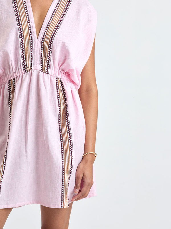 Close up on a Woman Standing wearing lemlem ALEM Dress featuring detailed bands of deep burgundy, bronze, and pink stripes beautifully placed on a light cream 