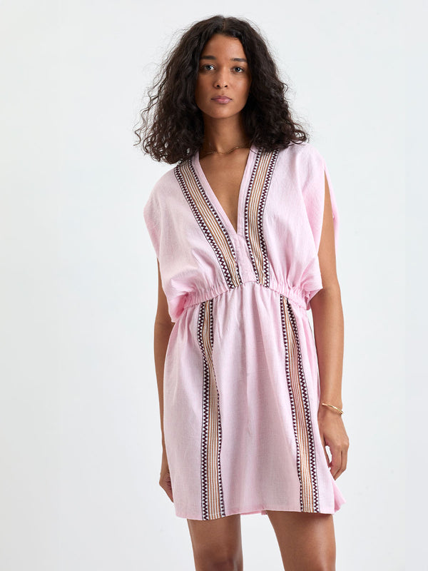 Woman Standing wearing lemlem ALEM Dress featuring detailed bands of deep burgundy, bronze, and pink stripes beautifully placed on a light cream 