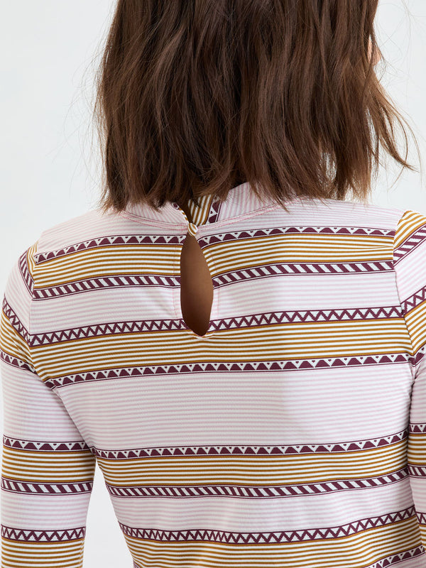 Close up on a back of a Woman Standing wearing lemlem AZEB Rash Guard and MERON Brief Bottom featuring detailed bands of deep burgundy, bronze, and pink stripes beautifully placed on a light cream 