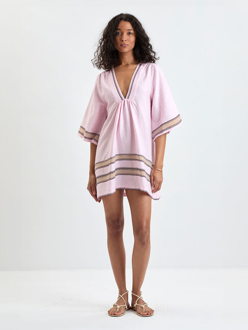 Woman Standing wearing lemlem BELKIS Caftan featuring detailed bands of deep burgundy, bronze, and pink stripes beautifully placed on a light cream 