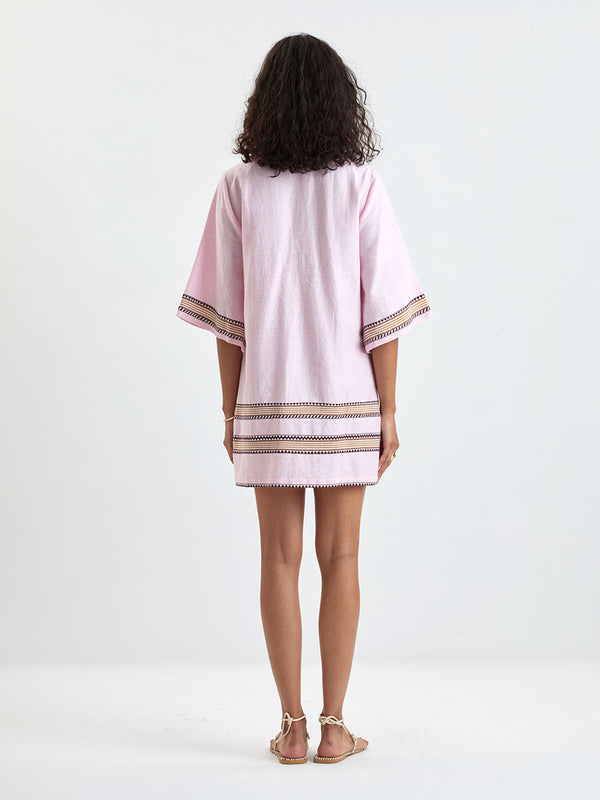 back of a Woman Standing wearing lemlem BELKIS Caftan featuring detailed bands of deep burgundy, bronze, and pink stripes beautifully placed on a light cream 