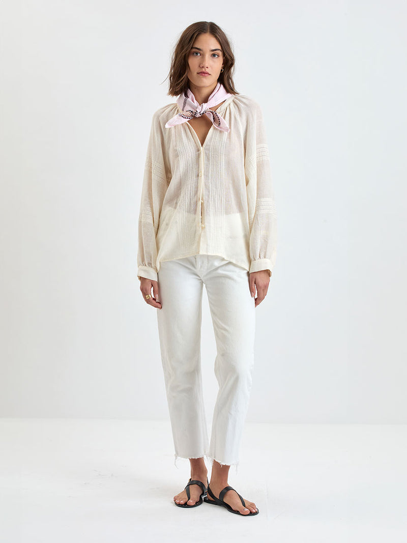 Woman wearing a light-colored blouse and white pants on a white background